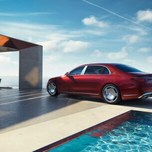 Ein roter Mercedes-Maybach von der Seite am Pool eines modernen Hauses, im Hintergrund Meer und Personen im Haus