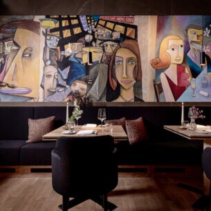 Tische und Bänke mit Kissen in einem Restaurant, an der Wand Malerei