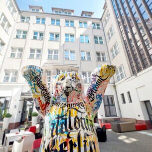 Die Statue eines bunten Berliner Bären steht im Innenhof eines mehrstöckigen weißen Hotels