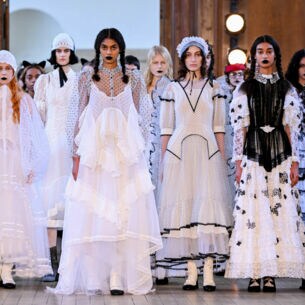 Models in langen, verspielten Kleidern in schwarz und weiß stehen nebeneinander auf dem Laufsteg einer Modenschau