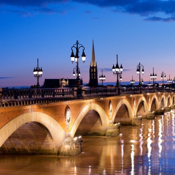 Eine alte Steinbrücke mit erleuchteten Straßenlaternen verläuft über einen Fluss in Bordeaux bei Nacht