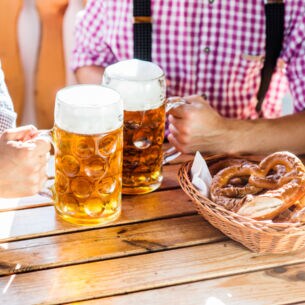 Nahaufnahme von zwei Männern, die an einem Tisch in einem Brauhaus mit zwei Maßkrügen Bier anstoßen
