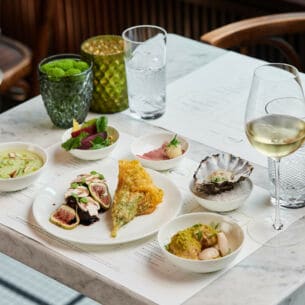 Mehrere Teller mit feinen Speisen und ein Glas Weißwein stehen auf einem Marmortisch