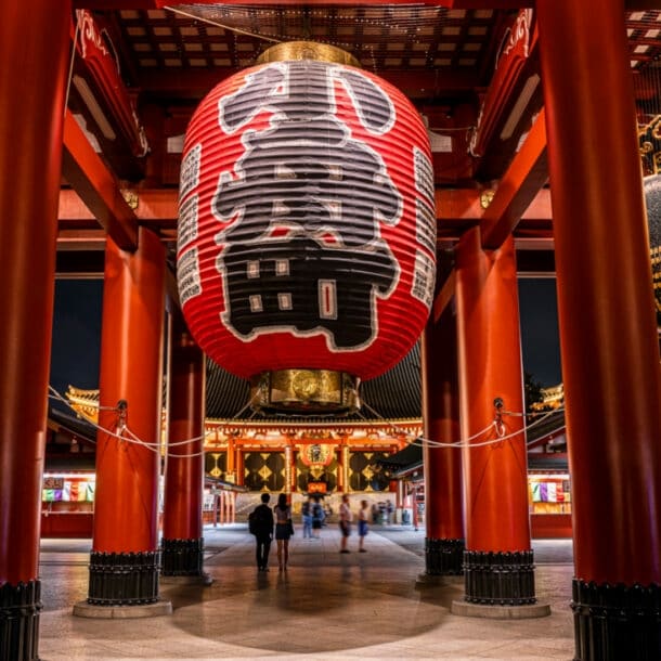 Rote Säulen und überdimensionale Laternen mit japanischen Schriftzügen in einem Tempel