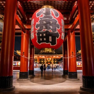 Rote Säulen und überdimensionale Laternen mit japanischen Schriftzügen in einem Tempel