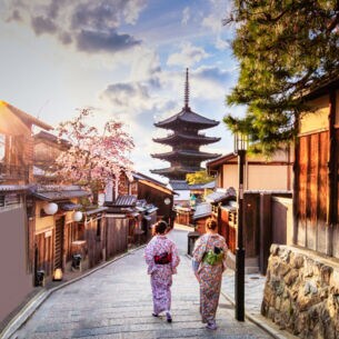 Zwei Frauen in bunten Kimonos laufen durch eine Gasse in der Altstadt von Kyoto auf einen Tempel zu