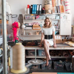 Marina Hoermanseder sitzt in ihrem Atelier auf ihrem Schreibtisch