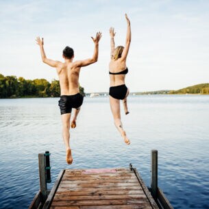 Rückansicht eines Paares in Badekleidung, das von einem Steg in einen See springt