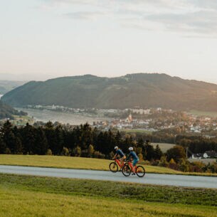 Zwei Radfahrer fahren auf dem Donauradweg mit Blick auf Berge
