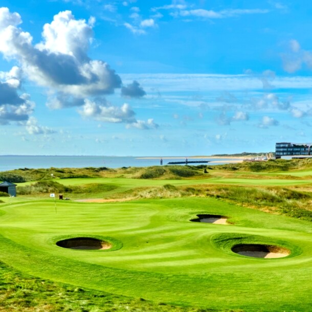 Grüner Golfplatz mit runden Bunkern mit Hotel und Meer im Hintergrund