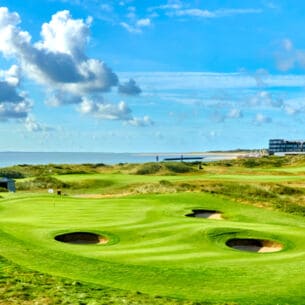 Grüner Golfplatz mit runden Bunkern mit Hotel und Meer im Hintergrund