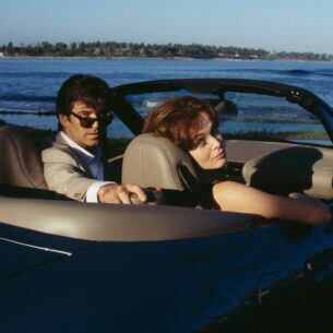 Schauspieler Pierce Brosnan mit Sonnenbrille sitzt neben einer Frau am Steuer eines Cabriolets