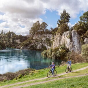 Ein Paar auf Fahrrädern fährt auf einem Radweg entlang eines Sees, umgeben von bewaldeten Felsen