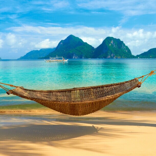 Eine Hängematte ist an einem Sandstrand vor türkisblauem Meer aufgespannt