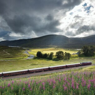 Ein Zug in einer grünen Hügellandschaft mit wolkigem Himmel