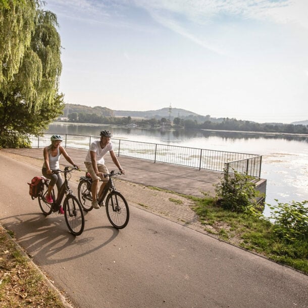 Ein Paar in Sommerkleidung fährt auf Fahrrädern auf einem Radweg entlang eines Flusses