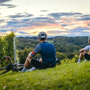 Rückenansicht zweier Personen in Fahrradkleidung, die auf einem Weinberg sitzen
