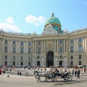 Personen und Pferdekutschen auf einem Platz vor der Wiener Hofburg