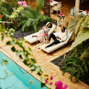 Aufsicht eines elegant gekleideten Paares auf Sonnenliegen an einem Pool auf der Terrasse eines Boutiquehotels.