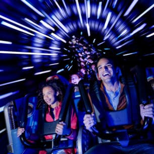 Ein Mann und ein Mädchen fahren fröhlich im Wagen einer Achterbahn durch einen dunklen Tunnel mit Lichteffekten