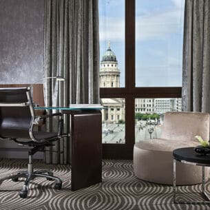 Luxuriöses Hotelzimmer mit Schreibtisch an einem bodentiefen Fenster mit Blick auf den Dom am Gendarmenmarkt in Berlin.