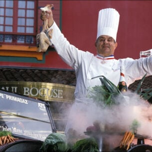 Paul Bocuse in Kochuniform bei einer Inszenierung mit Lebensmitteln vor seinem Restaurant
