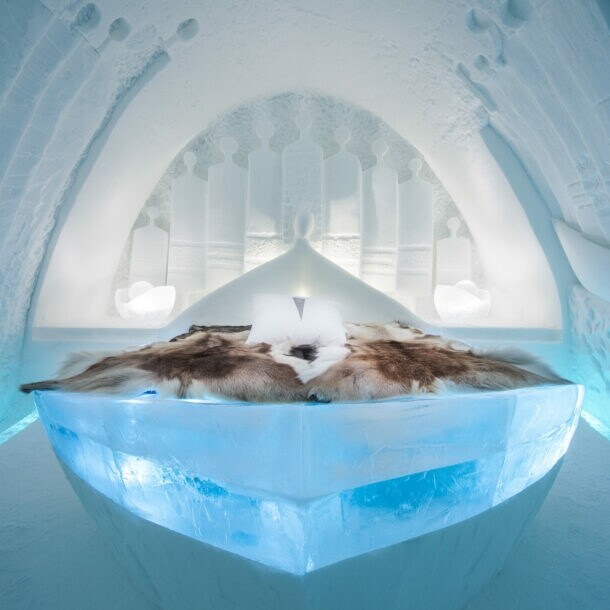 Innenansicht eines Zimmers in einem Eishotel mit Rentierfellen auf dem Bett.