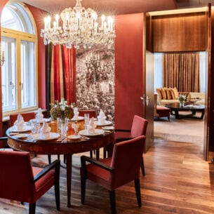 Runder, elegant eingedeckter Esstisch unter einem Kronleuchter in einer luxuriösen Suite in Terrakottatönen.