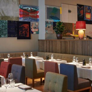 Restaurant mit Polsterstühlen an elegant gedeckten Tischen vor einer Wand mit farbenfrohen Gemälden.