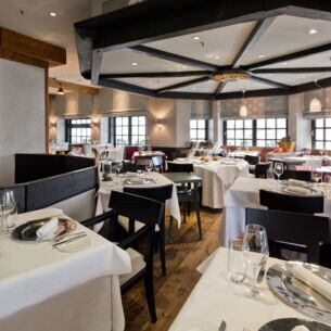 Elegantes Restaurant mit schwarzen Holzstühlen an eingedeckten Tischen mit weißen Tischdecken.
