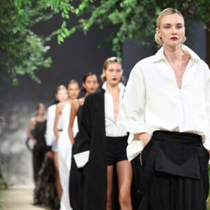 Weibliche Models in eleganter Kleidung mit klassischen Schnitten in den Farben Schwarz und Weiß auf einem Laufsteg bei einer Modenschau.