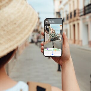 Eine Frau navigiert mit Blick auf ihr Smartphone per Live View von Google Maps durch eine Straße.