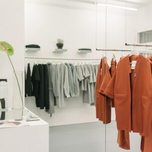 Puristische, elegante Kleidungsstücke, nach Farben sortiert, auf hängenden Kleiderstangen in einer Boutique.