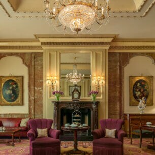 Edle, altehrwürdige Hotel Lobby Lounge mit Teppichboden, Goldverzierungen und roten Polstermöbeln unter einem Kronleuchter.