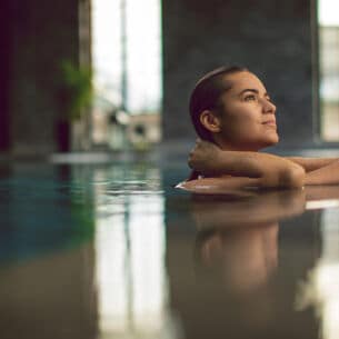Eine junge Frau entspannt am Beckenrand eines Pools in einem Wellnessbereich.