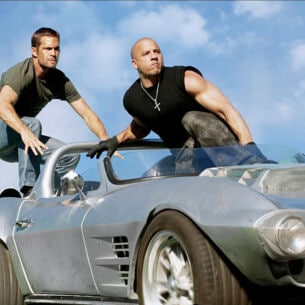 Paul Walker und Vin Diesel hocken auf einem silbernen Sportwagen ohne Verdeck.