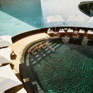 Aufsicht einer modernen Poollandschaft in einer exklusiven Hotelanlage mit Personen im Wasser.