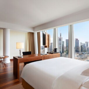Modernes Hotelzimmer mit Blick auf die Frankfurter Skyline durch bodentiefe Panoramafenster.