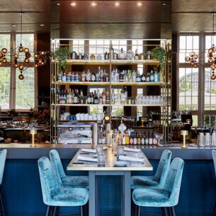 Verspiegelter Barbereich in einem modernen, edlen Restaurant mit blauen Samtstühlen an eingedeckten Tischen.