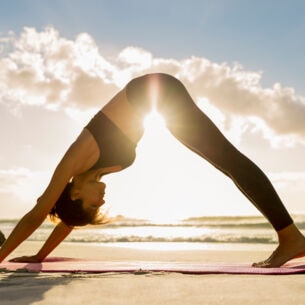 Eine Frau in einer Yoga-Pose am Strand. 
