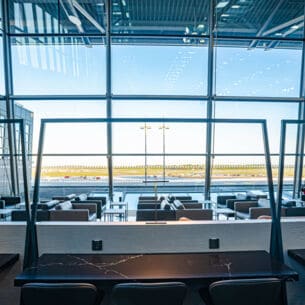 Leere Flughafen-Lounge mit Sitzmöbeln vor Panoramafenstern mit Blick aufs Rollfeld.