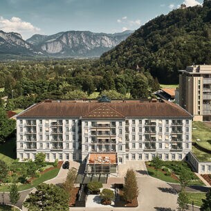 Luftansicht des Grand Resort Bad Ragaz in der Schweiz umgeben von grüner und waldiger Landschaft. Im Hintergrund Berge.