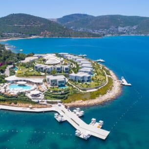 Luftaufnahme eines luxuriösen Hotelresorts mit weißen Bungalows auf einer Landzunge, umgeben von blauem Meer.
