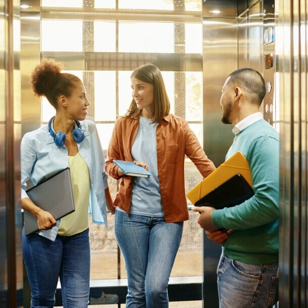 Drei Person stehen in einem Aufzug und unterhalten sich.