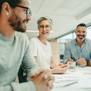 Kolleginnen und Kolleginnen diskutieren gutgelaunt am Besprechungstisch über ein Projekt.