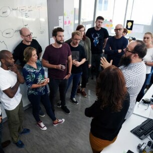 Ein diverses Business Team diskutiert miteinander vor einer Tafel.