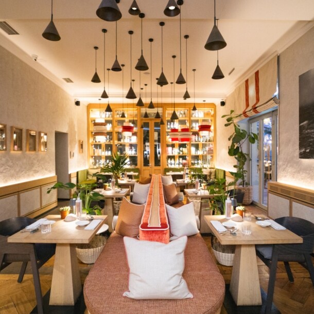 Hell ausgeleuchteter Innenraum des Restaurants Beetle von Feinkost Käfer in München mit Holztischen und einer Sitzbank im Mittelpunkt.