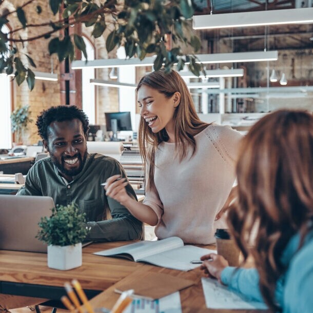 Drei junge Geschäftsleute unterhalten sich in einem hellen, modern eingerichteten Großraumbüro.
