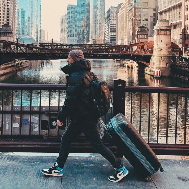 Ein junger Reisender mit Koffer und Rucksack überquert eine Brücke in Chicago.