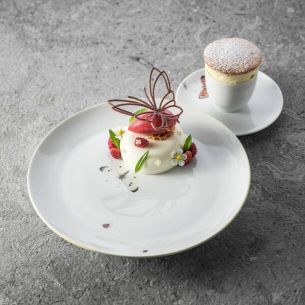 Stillleben zweier reduzierten, kunstvoll angerichteten Süßspeisen auf schlichten weißen Tellern auf anthrazitfarbenem Untergrund.